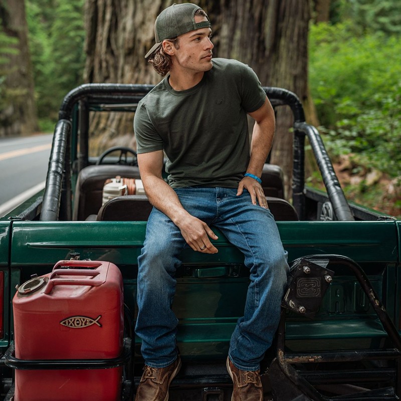 Max McNown sitting on the back of a green off-road vehicle in a forest