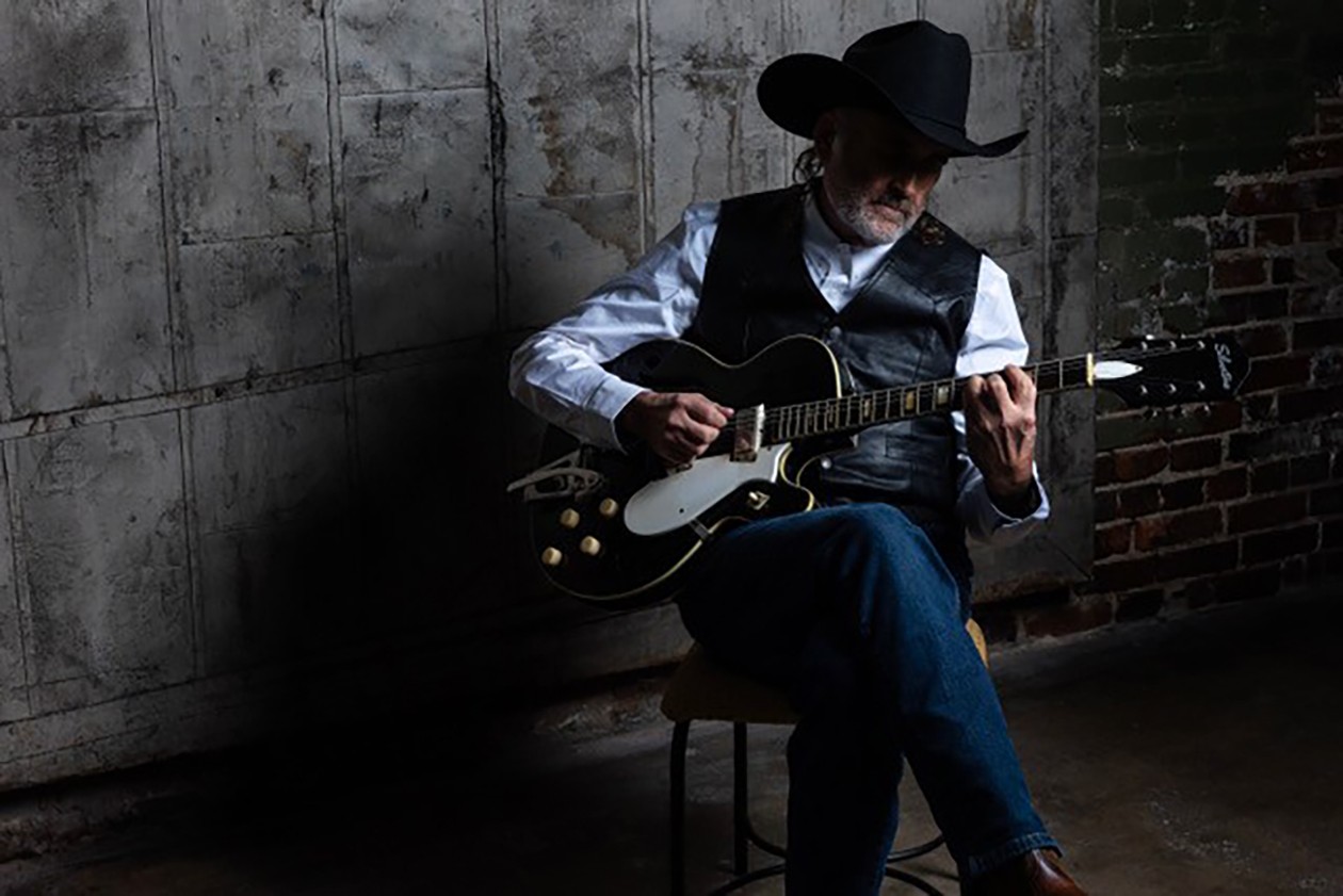 Randy Lee Riviere playing an electric guitar while wearing a black cowboy hat.
