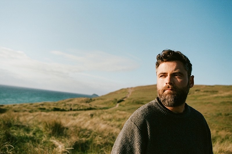 Passenger (Mike Rosenberg) outdoors in a coastal landscape, photographed for the Wild Love album campaign.